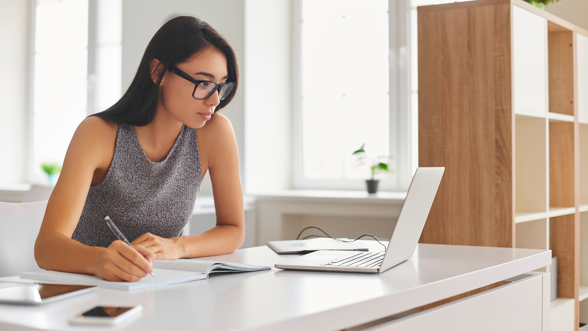 Frau Notizen anfertigend am Schreibtisch, Mobiltelefon und Laptop vor ihr ZEISS Academy